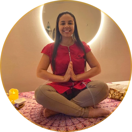 Massoterapeuta Liane Vieira sorrindo em posição de meditação com as mãos juntas em seu espaço de massoterapia em Brasília.